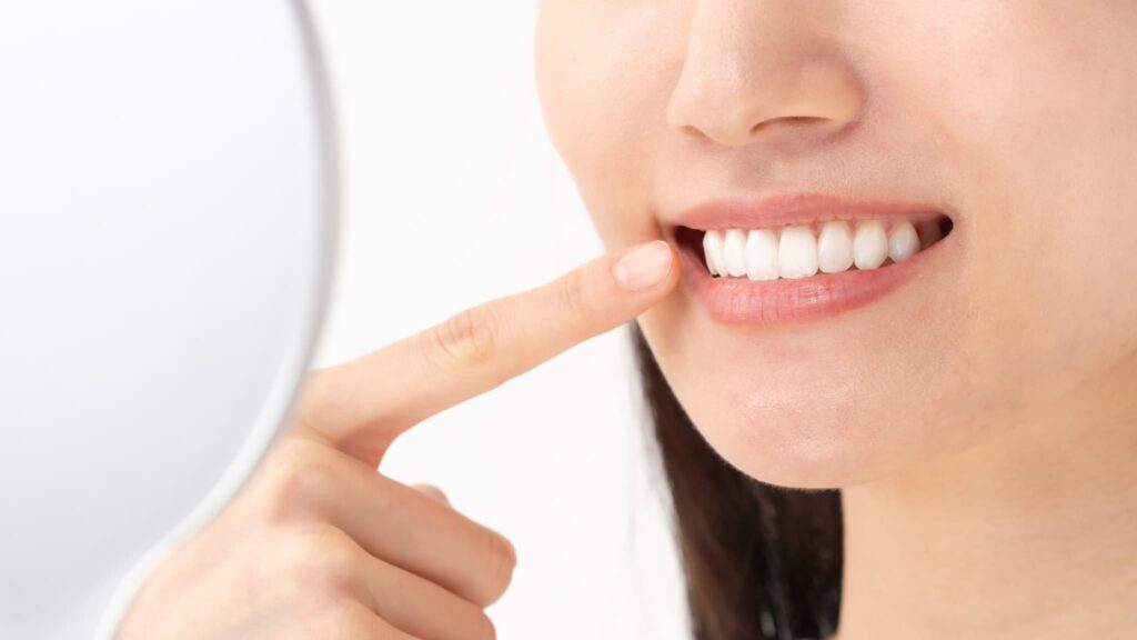 ホワイトニングした白い歯を指さす手鏡を持った女性